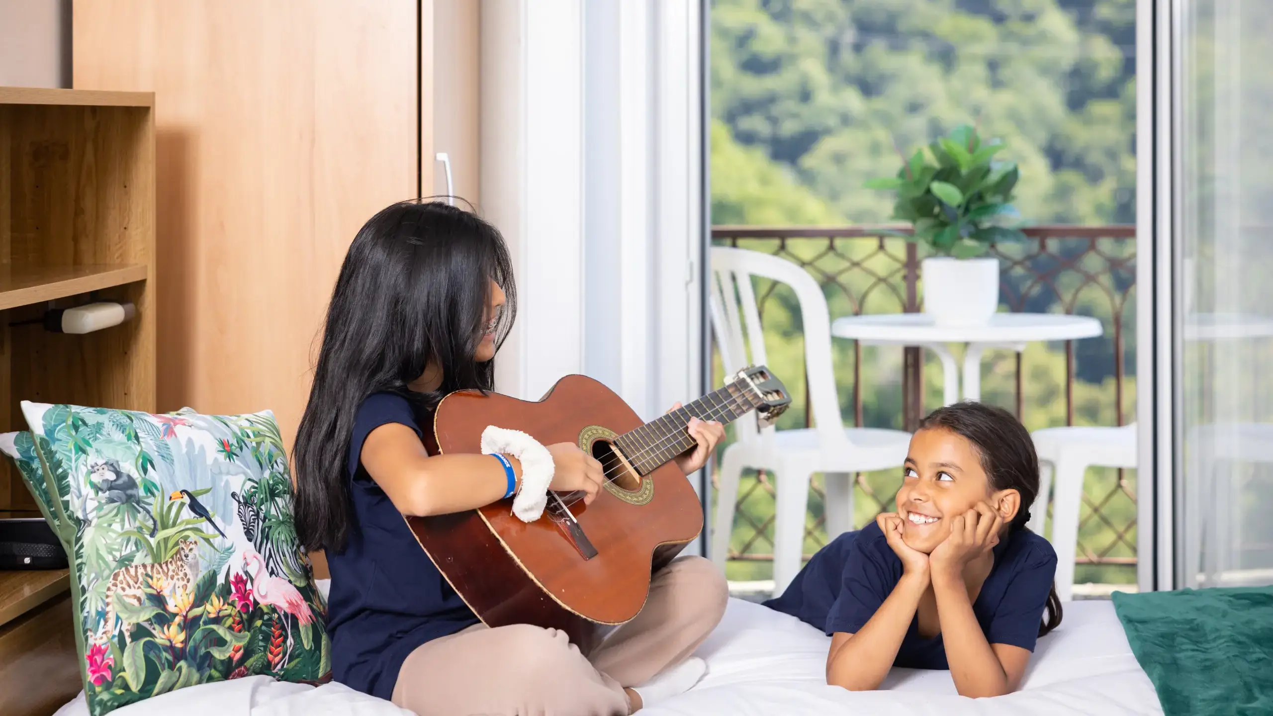 two girls sitting on bed playing guitar